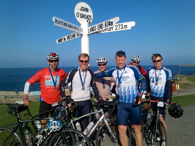 Cyclists fundraising for The Brain Tumour Charity, posing near a sign for a photo.