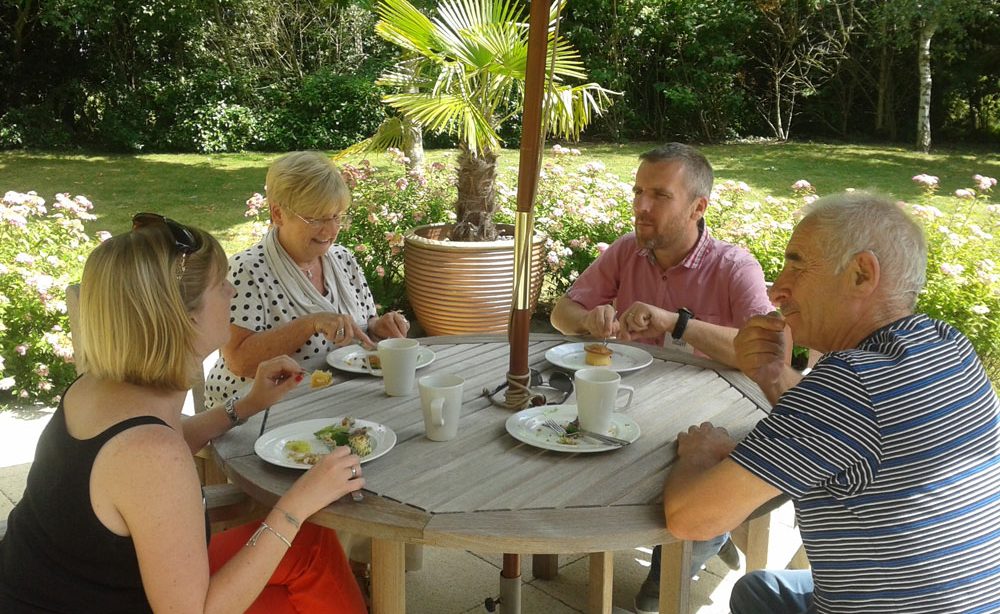 A family sitting comfortably around a picnic table as they chat about how they can better support their mum who has recently been diagnosed with a brain tumour.