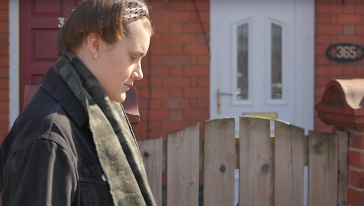 a woman in a coat and scarf walks down a British street