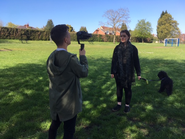 Two people film a video in a park, representing the YouTube channel of the Young Adults Service offered by The Brain Tumour Charity 