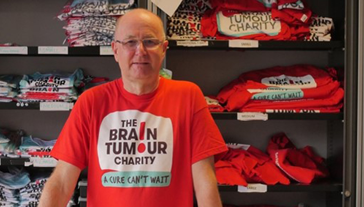 A man standing in front of a shelf full of t-shirts and hoodies as he volunteers at The Brain Tumour Charity HQ