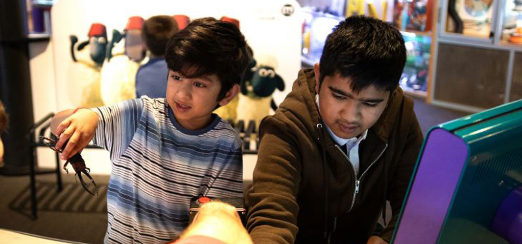 Two young boys gleefully explore the Science Museum together. The youngest holds a toy stag beetle.