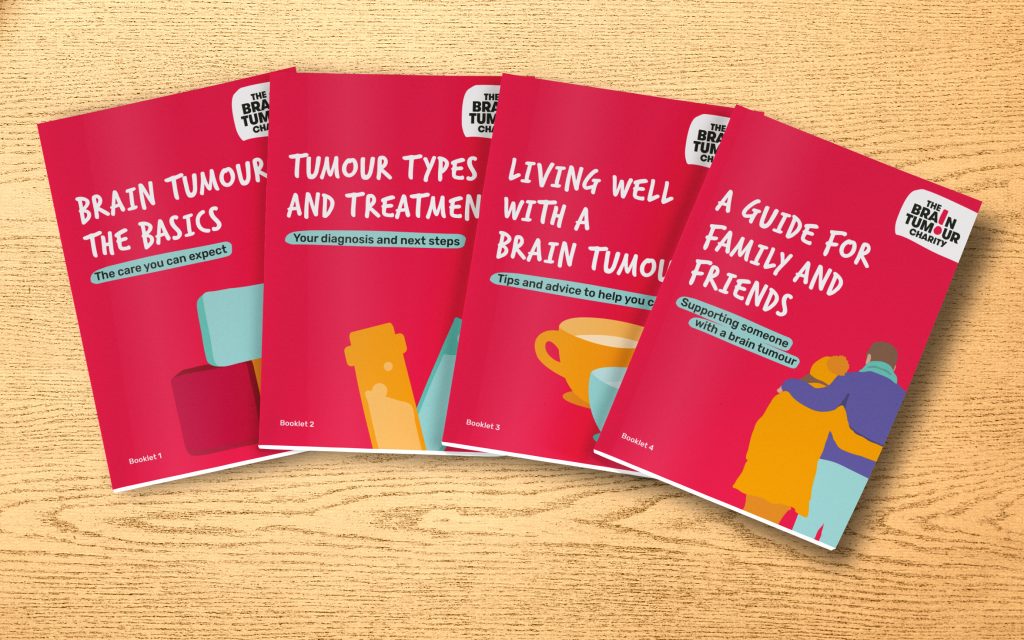 The four booklets that make up our Brain Tumour Information Pack are spread across a wooden desk. They're titled - "Brain Tumours:The Basics", "Tumour types and treatments", "Living well with a brain tumour" and "A guide for family and friends".