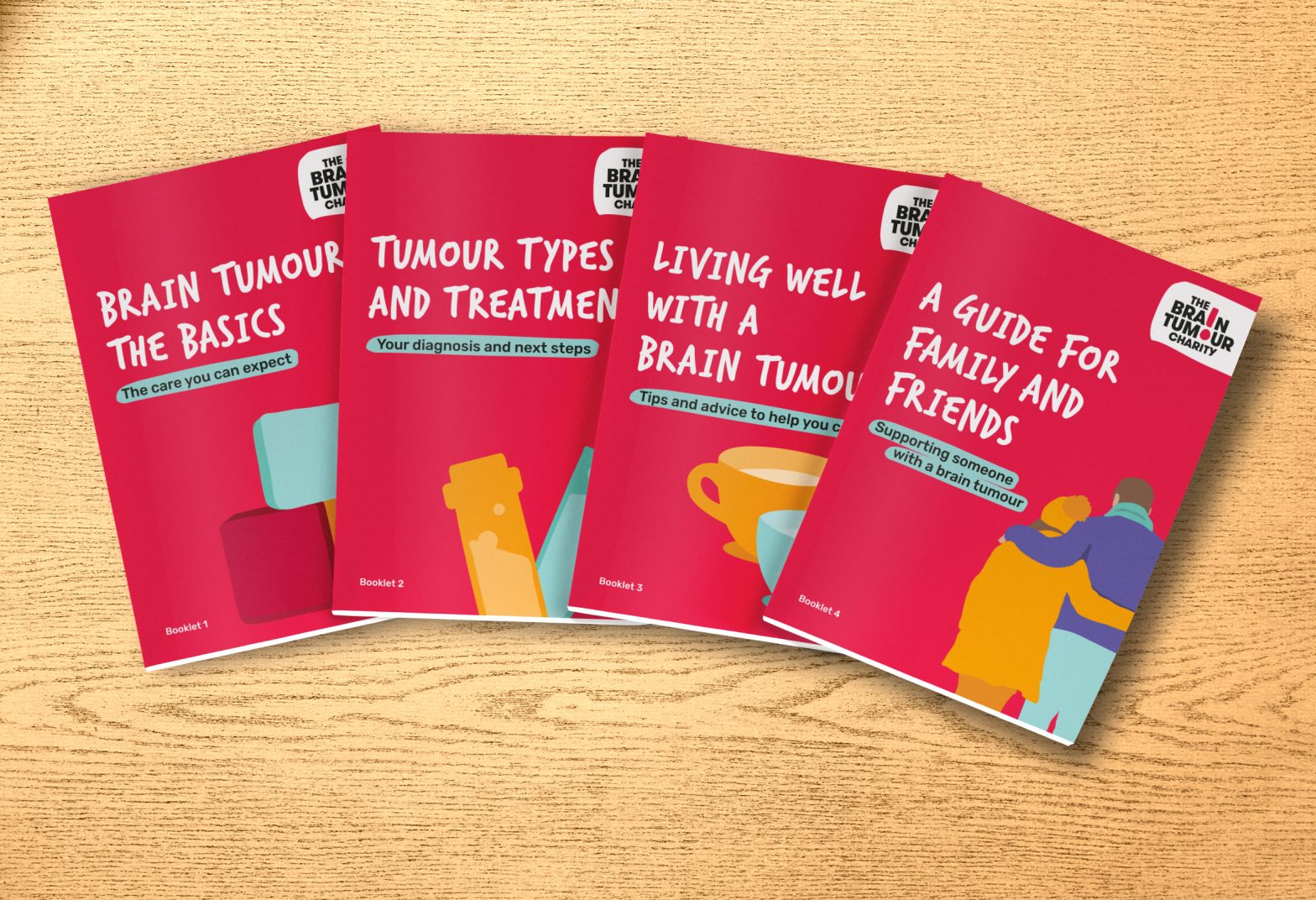 The four booklets that make up our Brain Tumour Information Pack are spread across a wooden desk. They're titled - "Brain Tumours: The Basics", "Tumour types and treatments", "Living well with a brain tumour" and "A guide for family and friends".