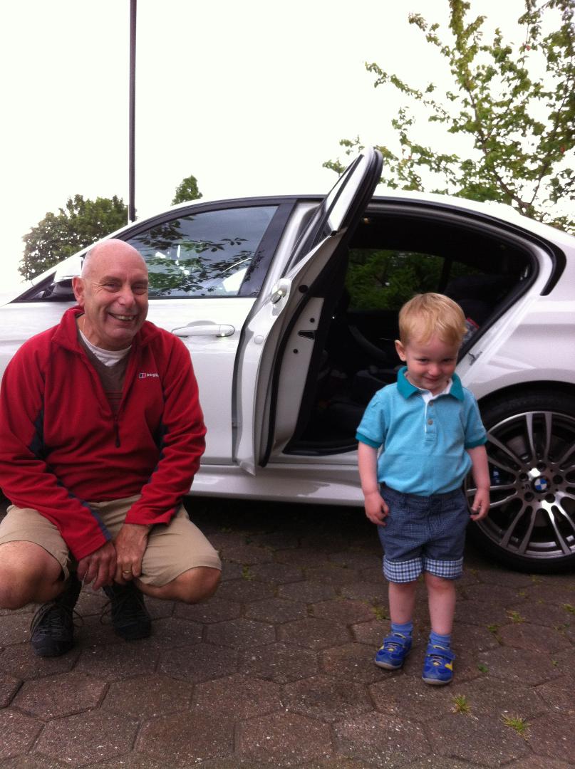 A man kneeling next to a young boy in front of a white car.