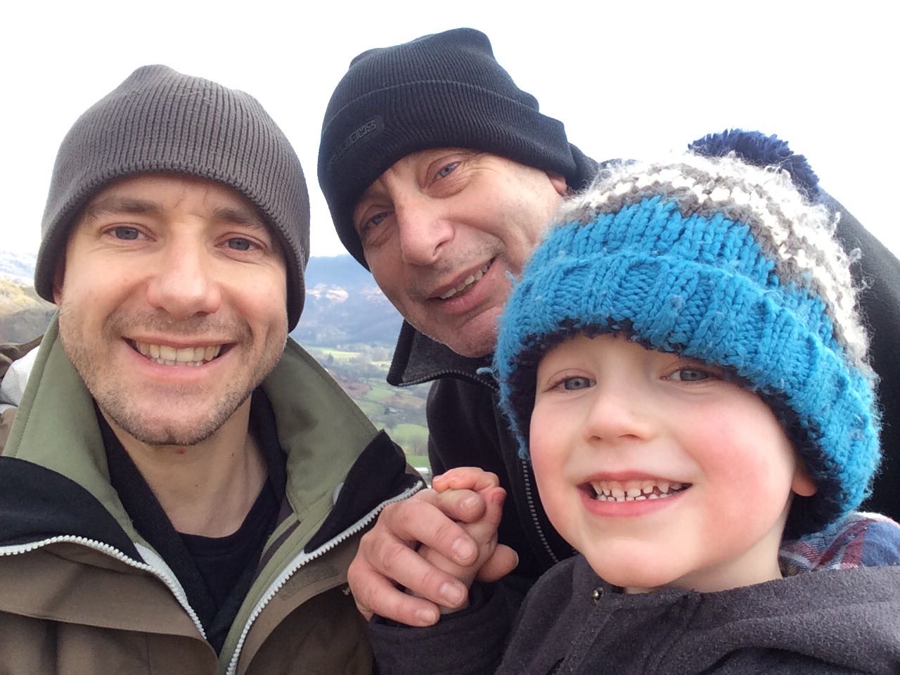 Two men and a young boy wearing wooly hats, smiling at the camera