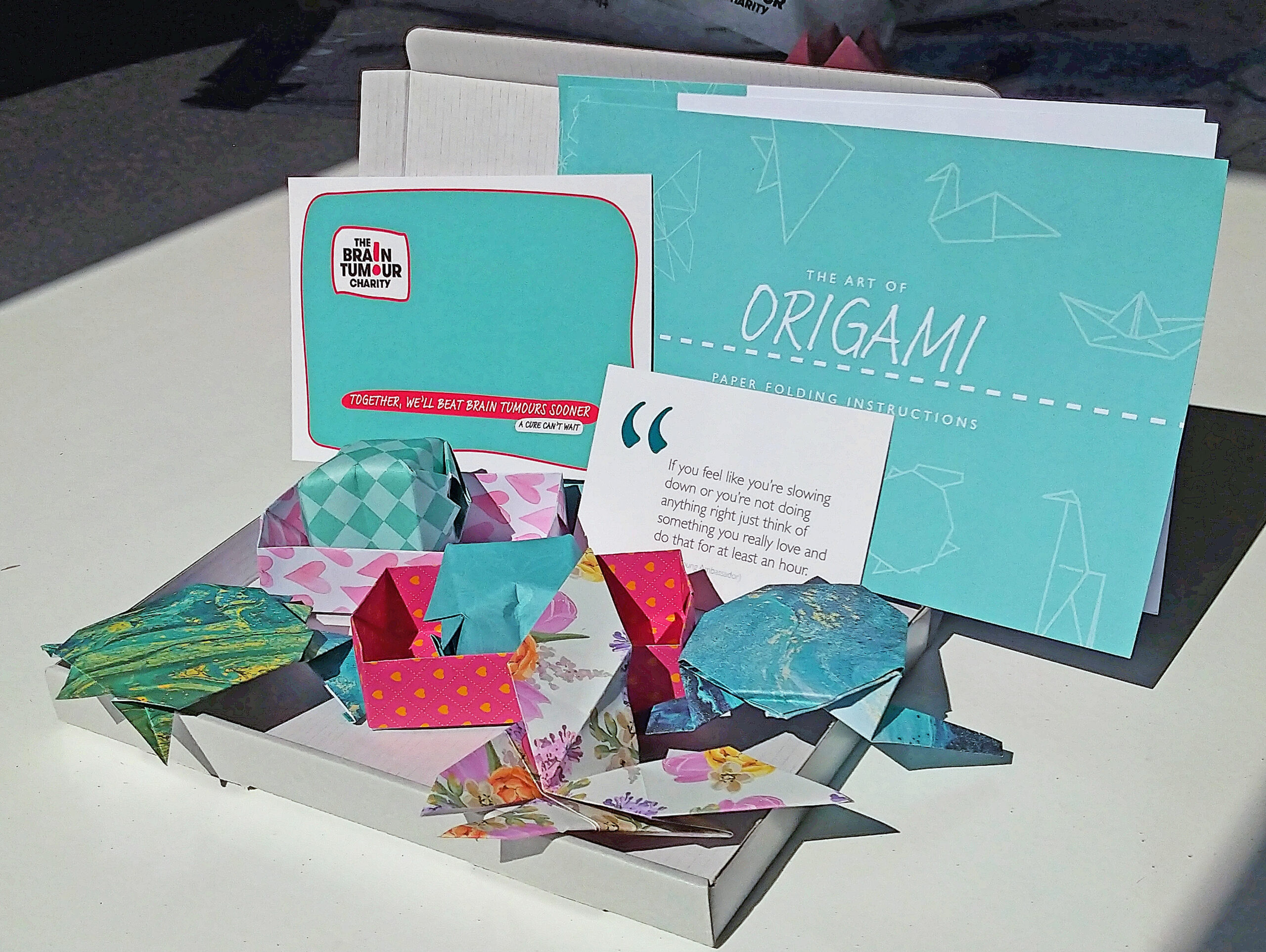 Piture of a small box on a white table with some paper folded into shapes to look like animals, a welcome card and instructions