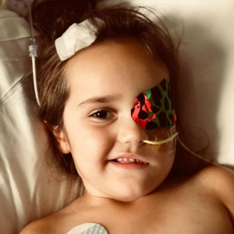 Ella lying bed with an eye covering and medical tubes around her