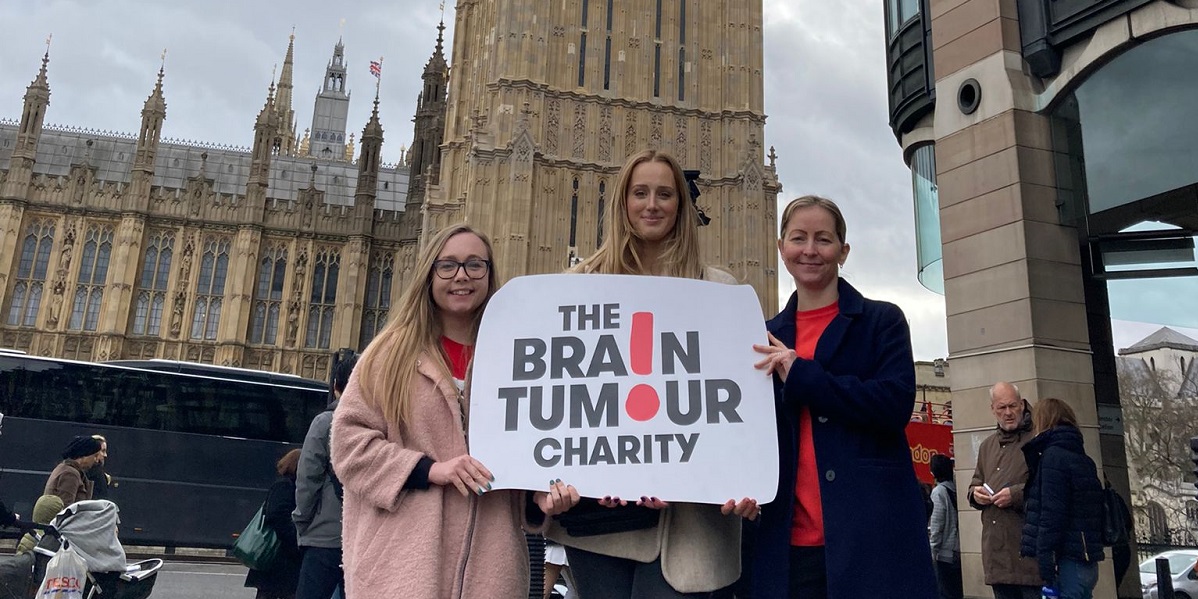 People hold a Brain Tumour Charity poster in front of the houses of parliament in Westminster as they campaign for faster diagnosis