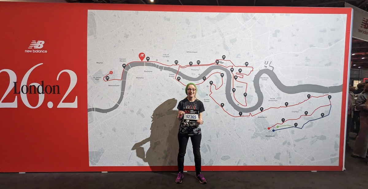 Camilla Hawkins standing in front of a London Marathon map holding her race number