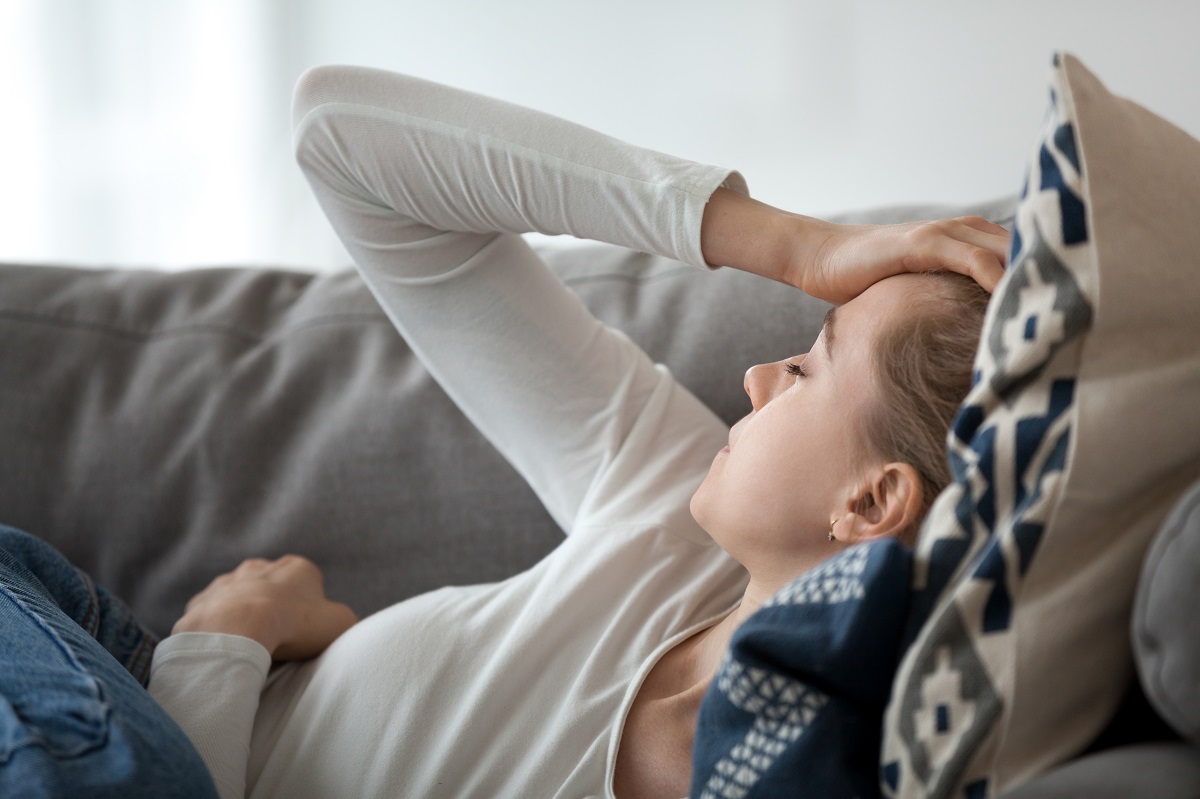 Woman with headache lying on a grey sofa with her hand on her head