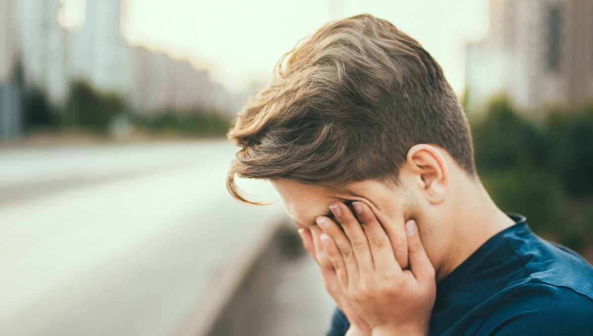 person standing next to a road with their head in their hands suffering from brain tumour fatigue