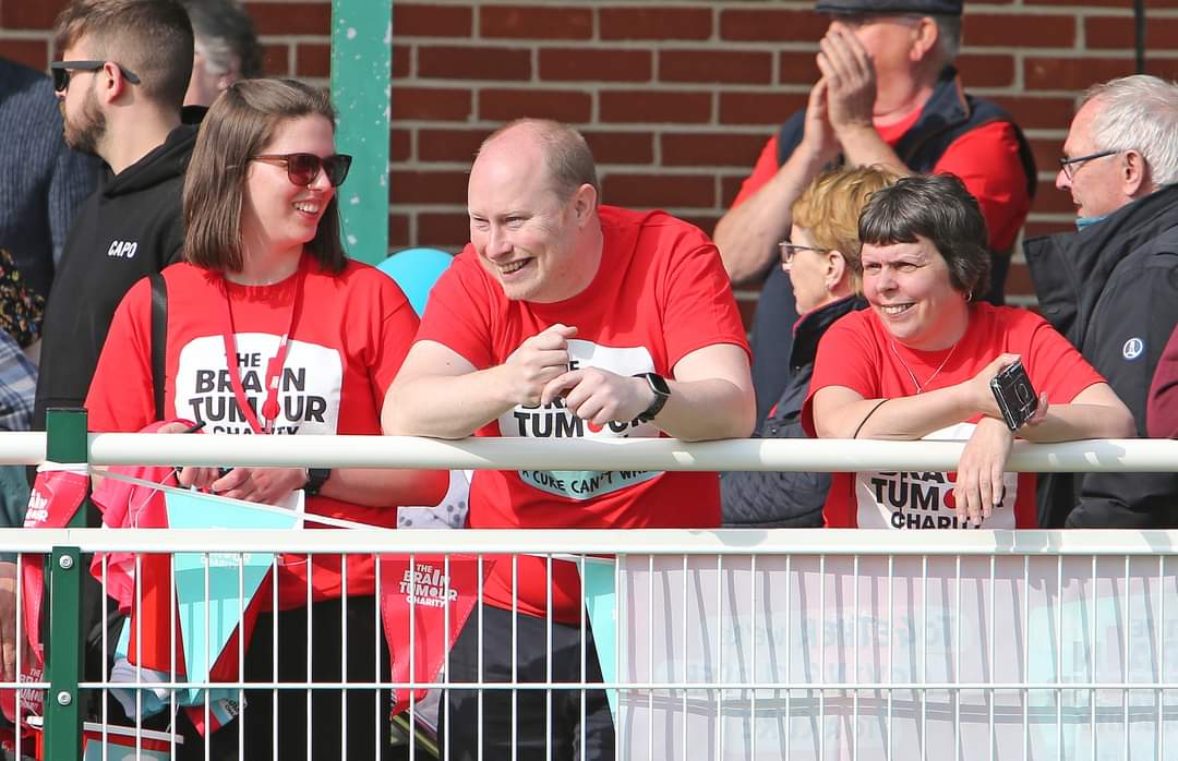 Madi, a Young Ambassador for The Brain Tumour Charity, and two other spectators watching the football match and smiling