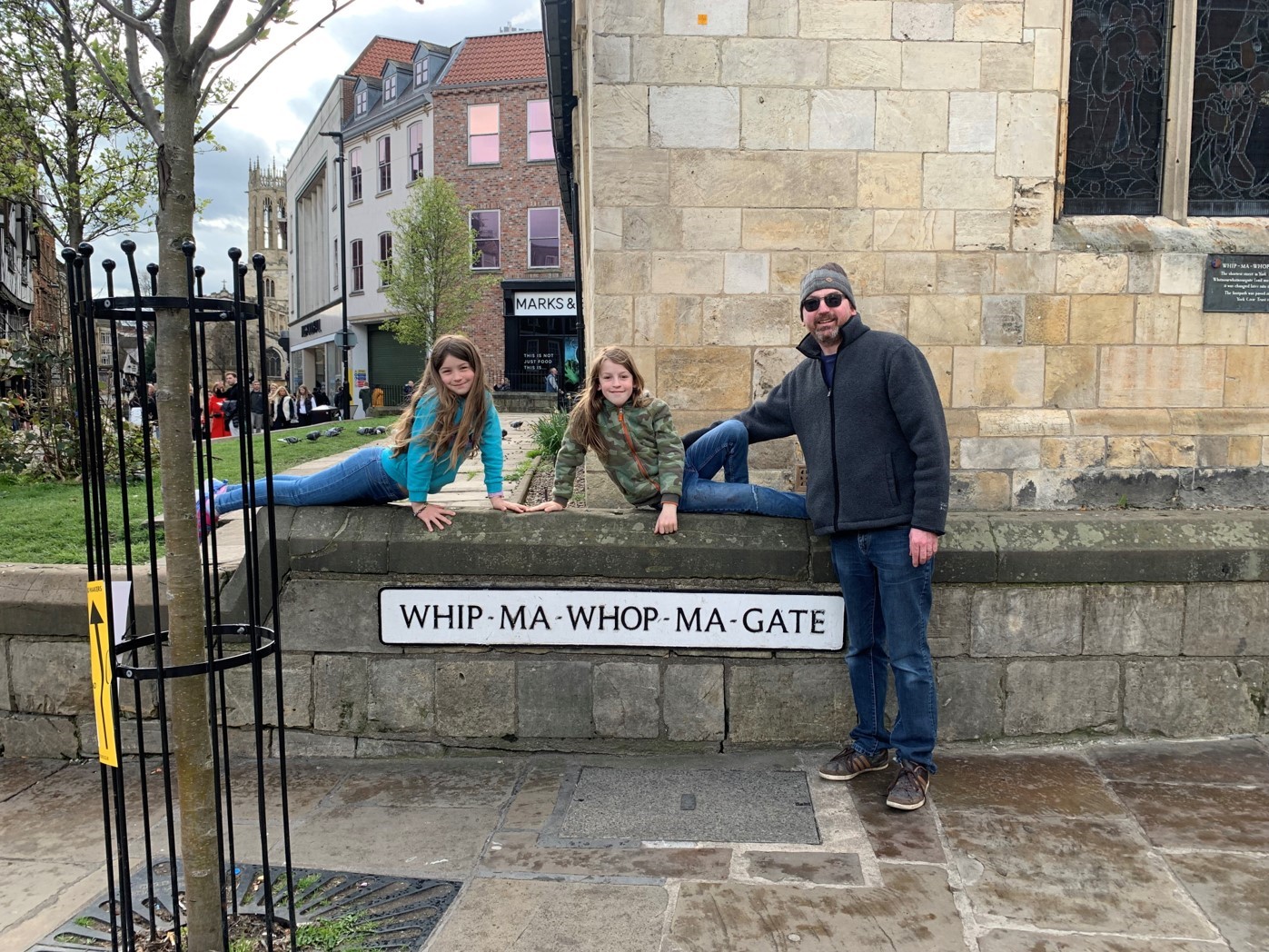 Peter with his children leaning against a wall by a sign that says: WHIP-MA-WHOP-MA-GATE. Peter died from a glioblastoma in 2022.