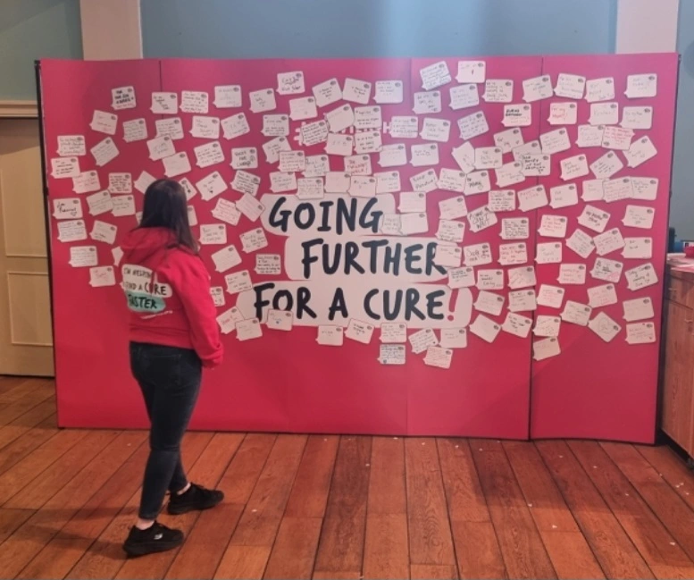 Lauren turned away from the camera looking at a message board that says Going Further for a Cure!