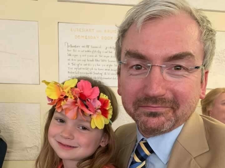 Peter and his daughter. Peter is dressed in a suit and his daughter is wearing a yellow and pink flowered headband. 