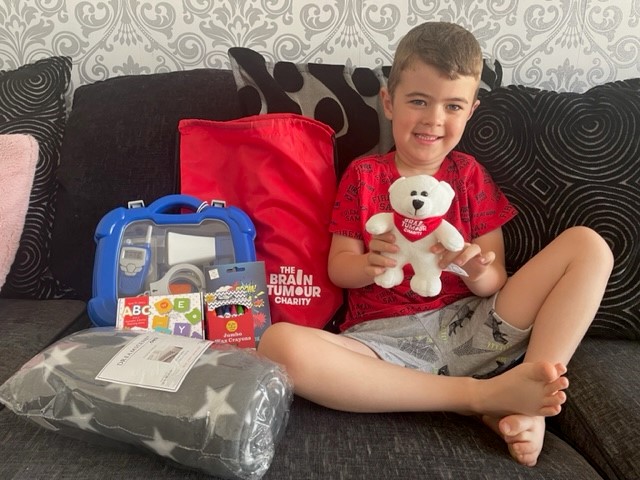 a young boy sits on a sofa holding a teddy bear