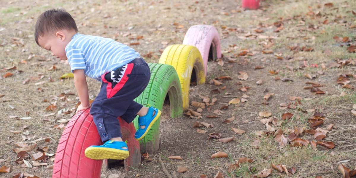 A child experiences balance problems while climbing over a tyre in a playground