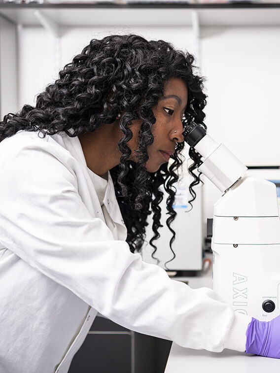 Sigourney in white coat using lab equipment