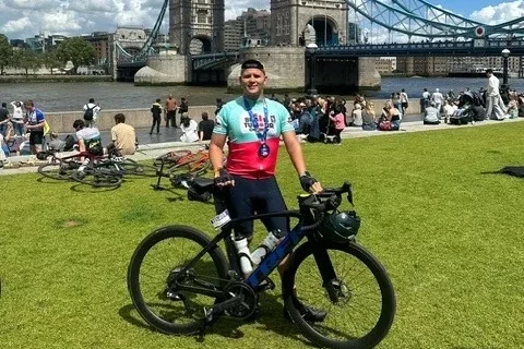 A cyclist holding his bicycle and standing in front of Tower Bridge for the London to Brighton Cycle