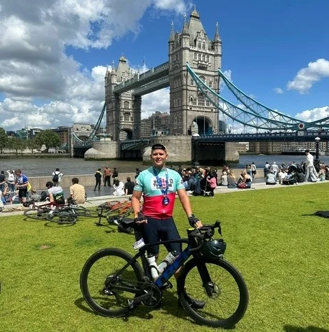 A cyclist holding his bicycle and standing in front of Tower Bridge for the London to Brighton Cycle