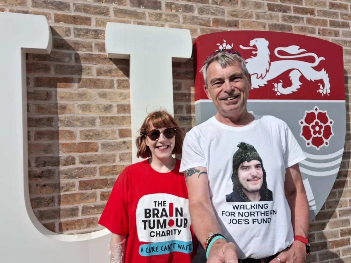 Richard and Evie stand in front of the Lancaster University logo during a fundraising event