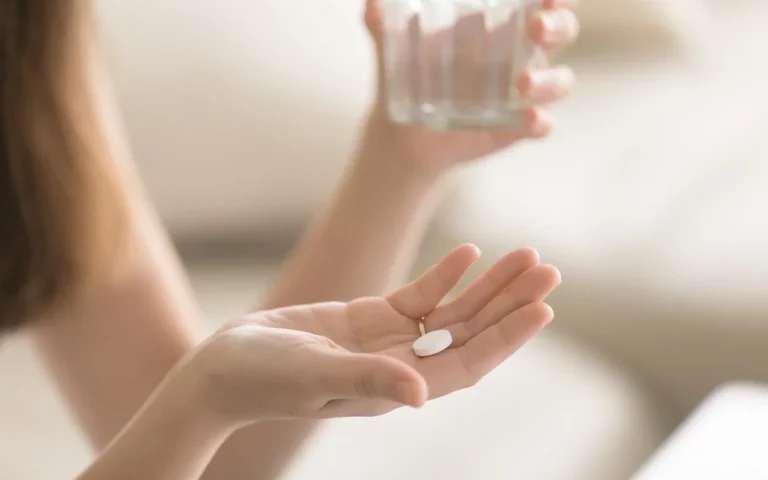 Hands holding a pill and a glass of water as the person takes part in a clinical trial for brain tumours