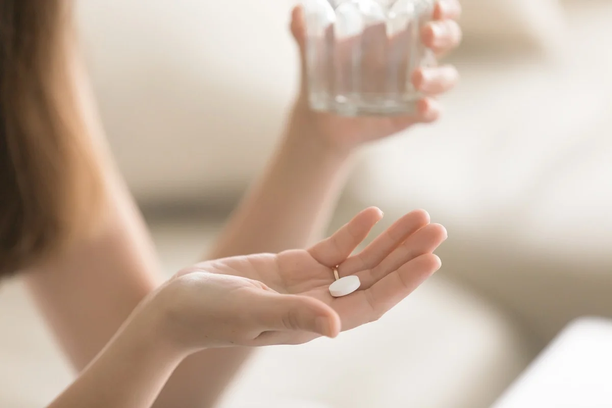 Hands holding a pill and a glass of water.