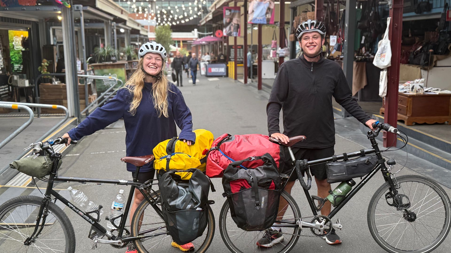 Jeremy and Lottie stand with their bicycles in a street. They'll be cycling from Australia to UK for charity