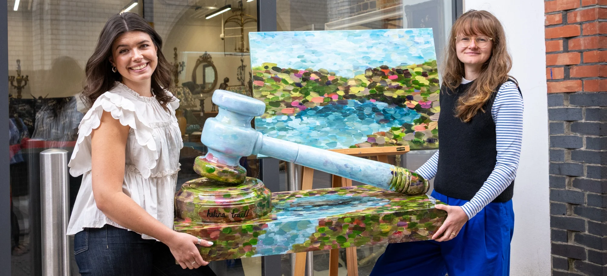 Artist Helena Traill and auctioneer specialist Ellie Smith hold a gavel sculpture up for auction