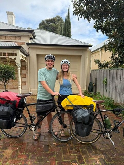 Jeremy and Lottie stand with their bikes in the driveway of a house