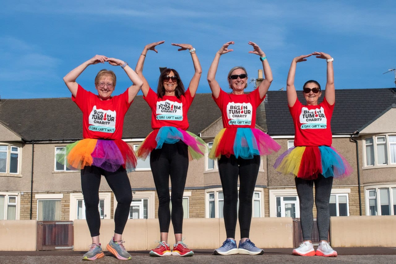 four ladies in colourful tutus wearing the brain tumour charity t-shirts with their arms above their heads