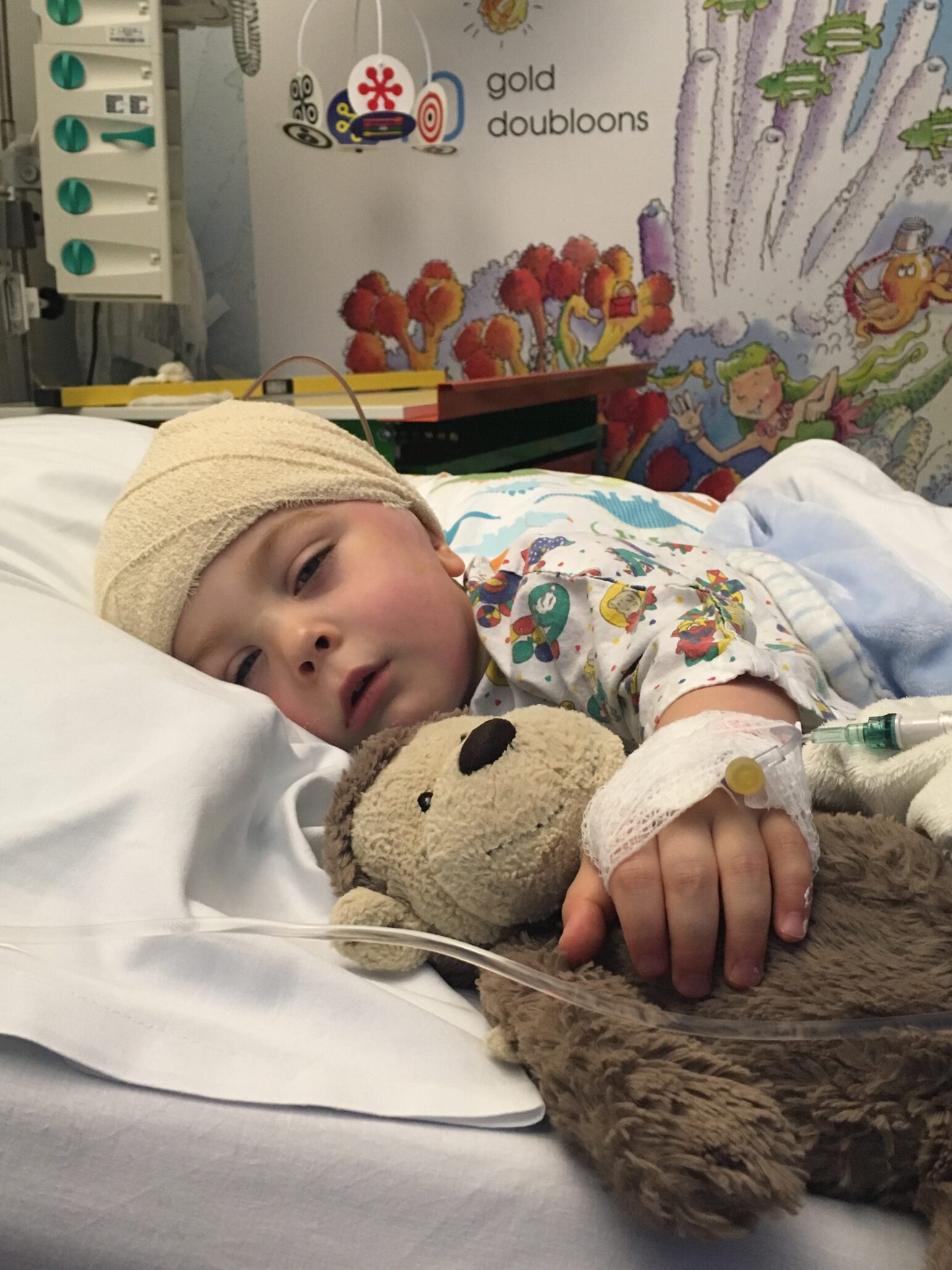 Arthur lies in a hospital bed with his head wrapped in bandages, cuddling a monkey toy.