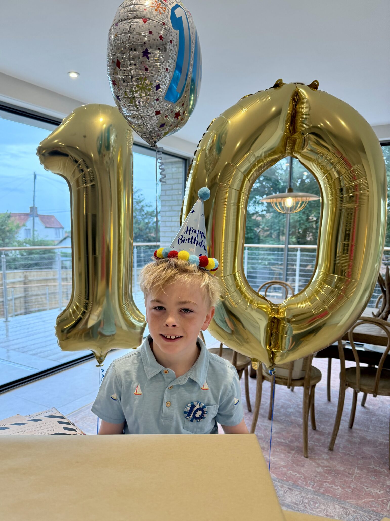 Arthur smiles at the camera with a birthday hat on, and birthday balloons in the shape of the number 10 behind him.