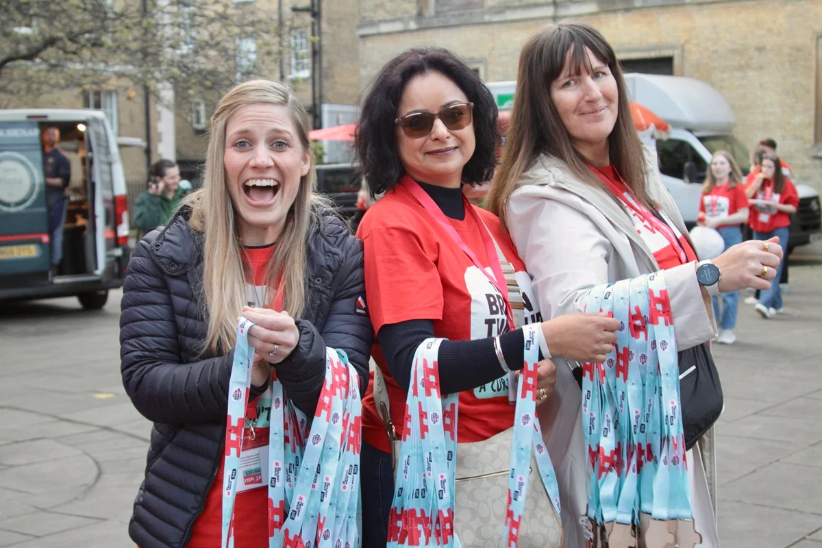 Three volunteers stand with arms full of medals at The Twilight Walk