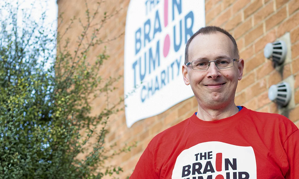 A volunteer for The Brain Tumour Charity stands outside the building. Volunteering is a good way to get involved with The Charity