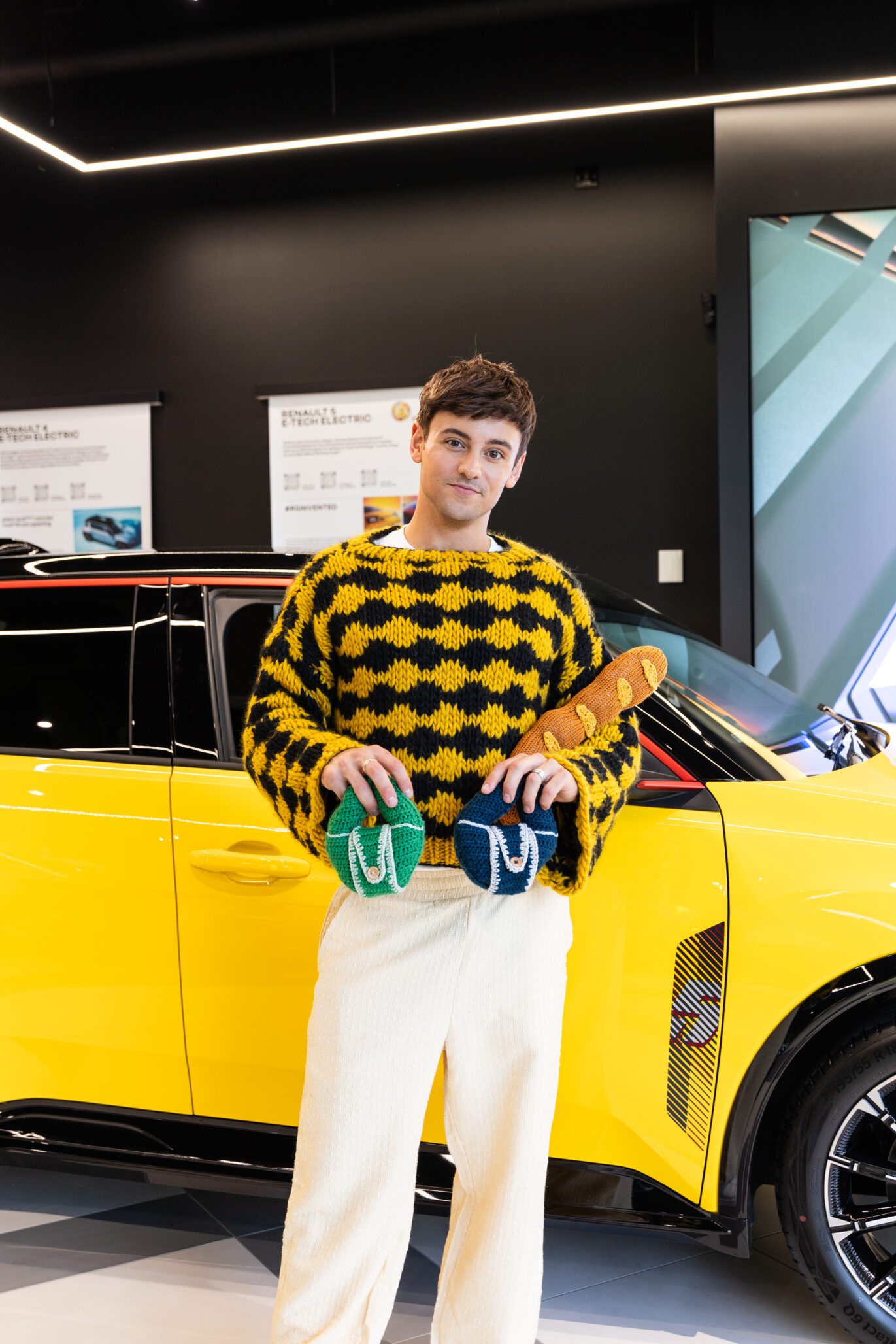 Tom Daley in front of a Renault holding a knitted baguette and croissants  