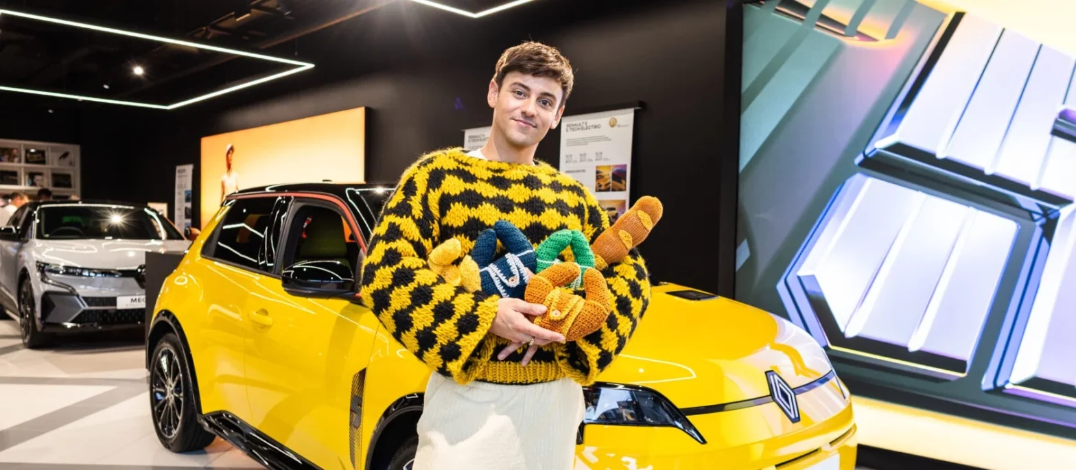 Tom Daley in front of a Renault car holding knitted baked goods