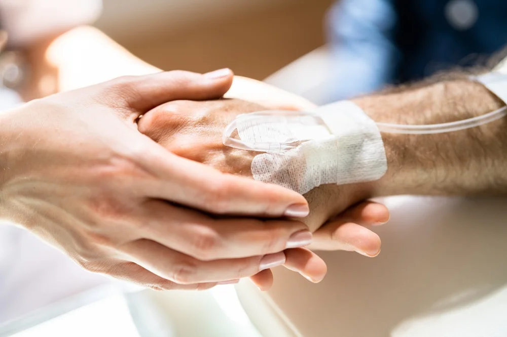 Hands holding a hand that has a drip and bandage on it