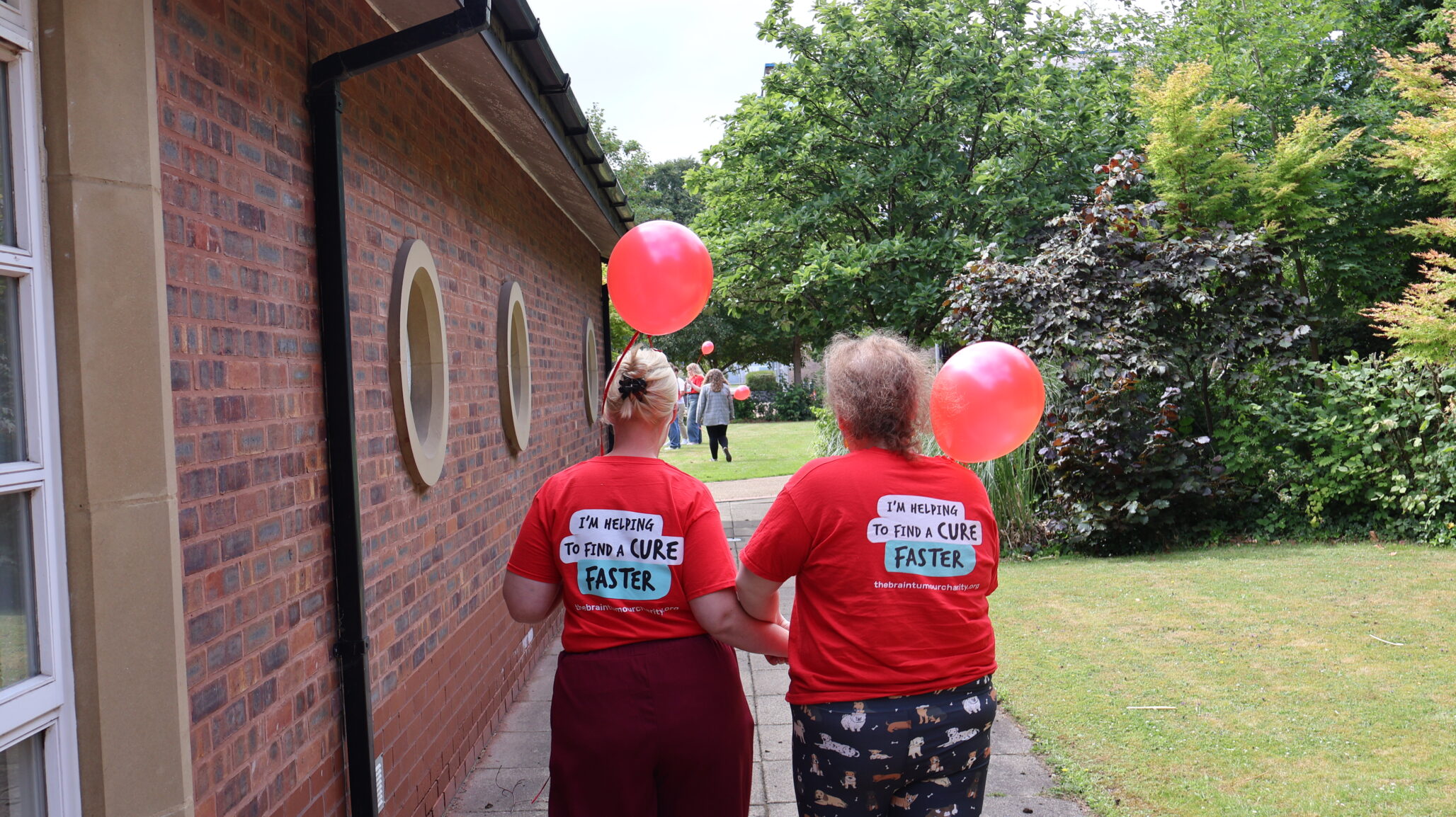 Two women walk away from the camera holding balloons