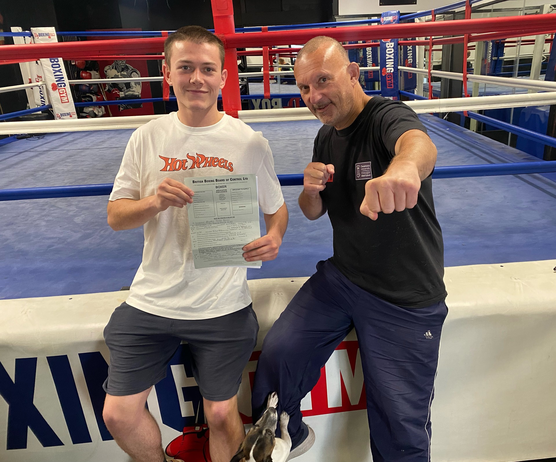 Ewan and his boxing coach sit on the side of a boxing ring. Ewan is running the entire border of Wales in memory of his grandfather