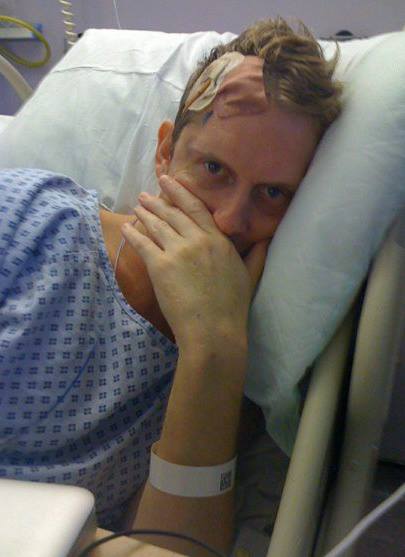 Rod Buchanan lies in a hospital bed on his side with a bandage over his head where his tumour was removed