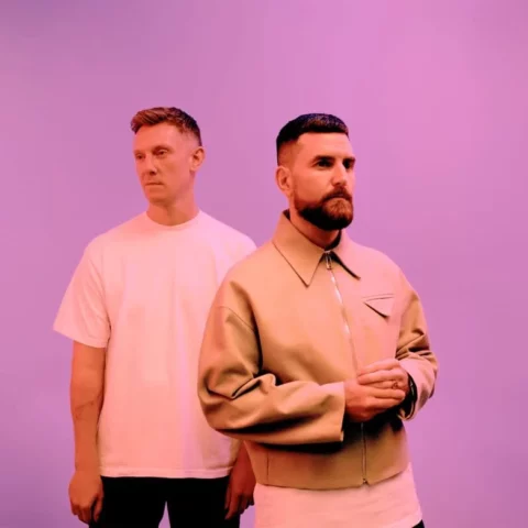 The members of Bicep, the electronic musical duo, stand looking off at different angles with a purple background