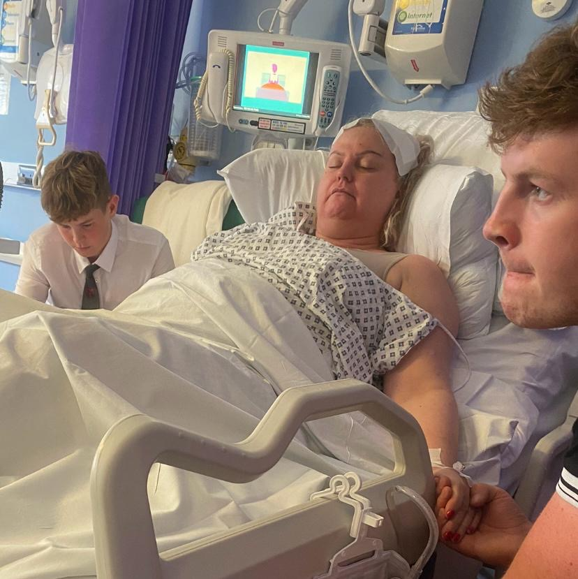 Claire lies in a hospital bed with her sons either side of her