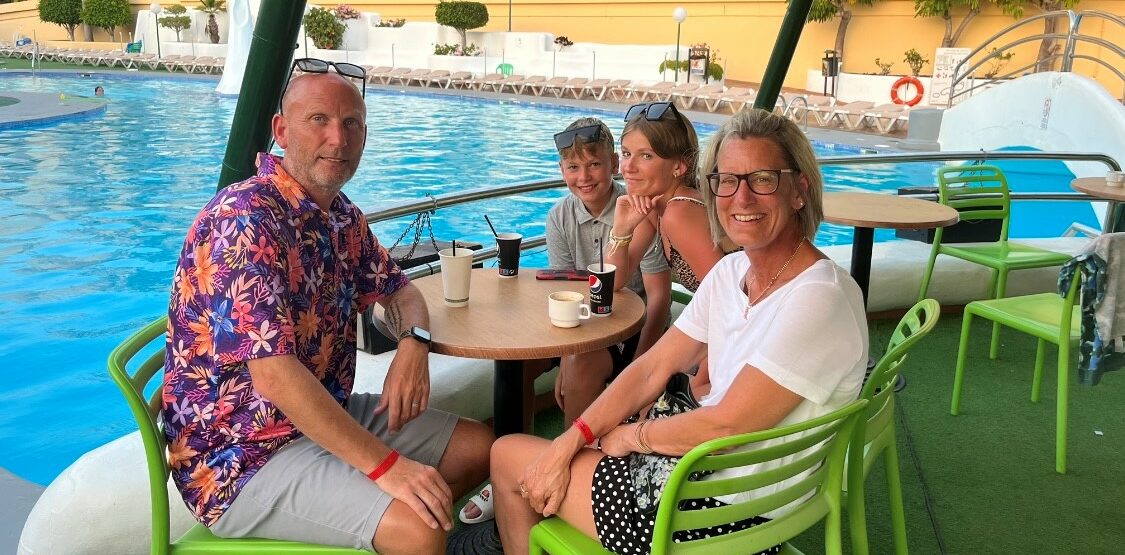 Gavin and family sit at green tables and chairs by a pool