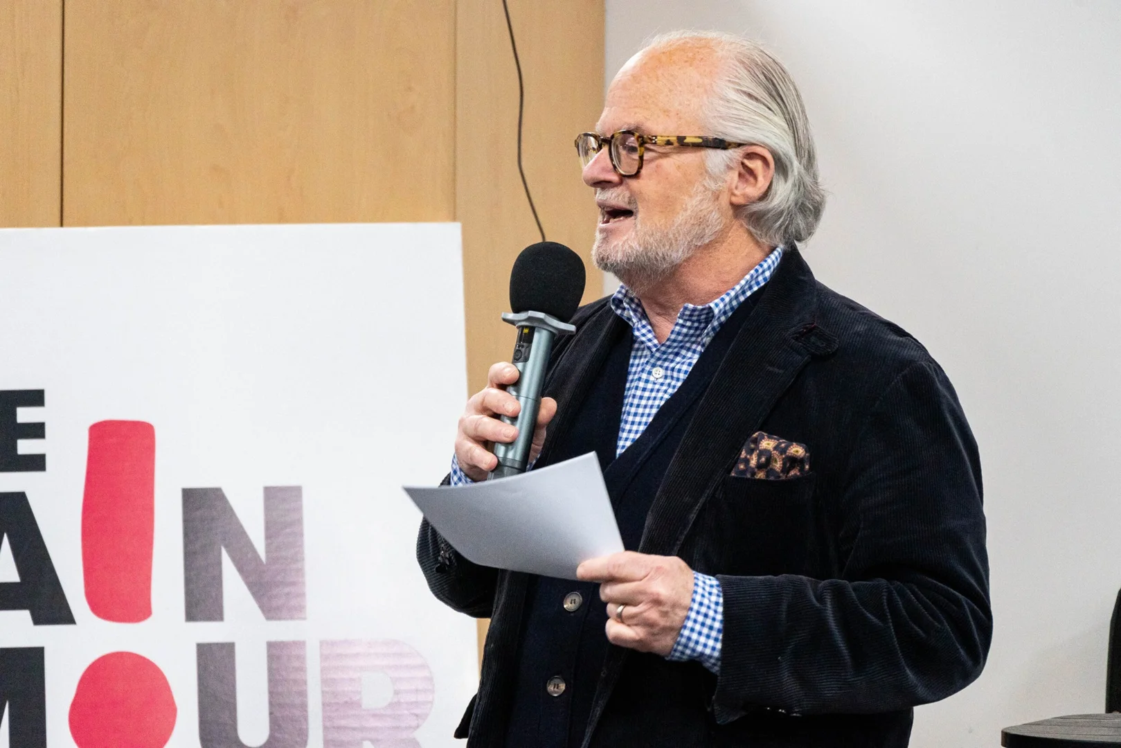 Jack Morris, former Chair of Trustees, speaks into a microphone in front of a sign for The Brain Tumour Charity