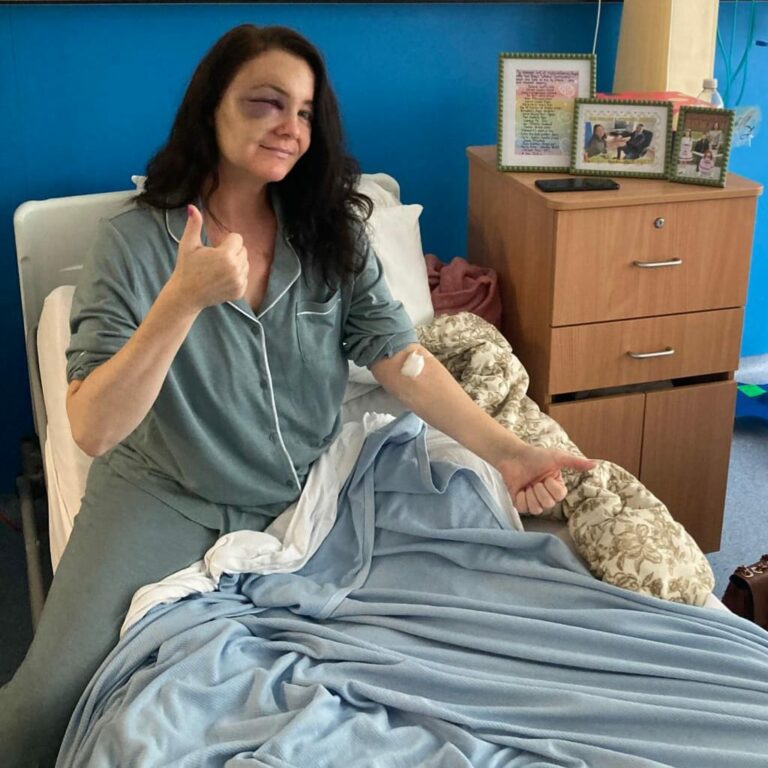 Julie sits up in her hospital bed and gives the thumbs up