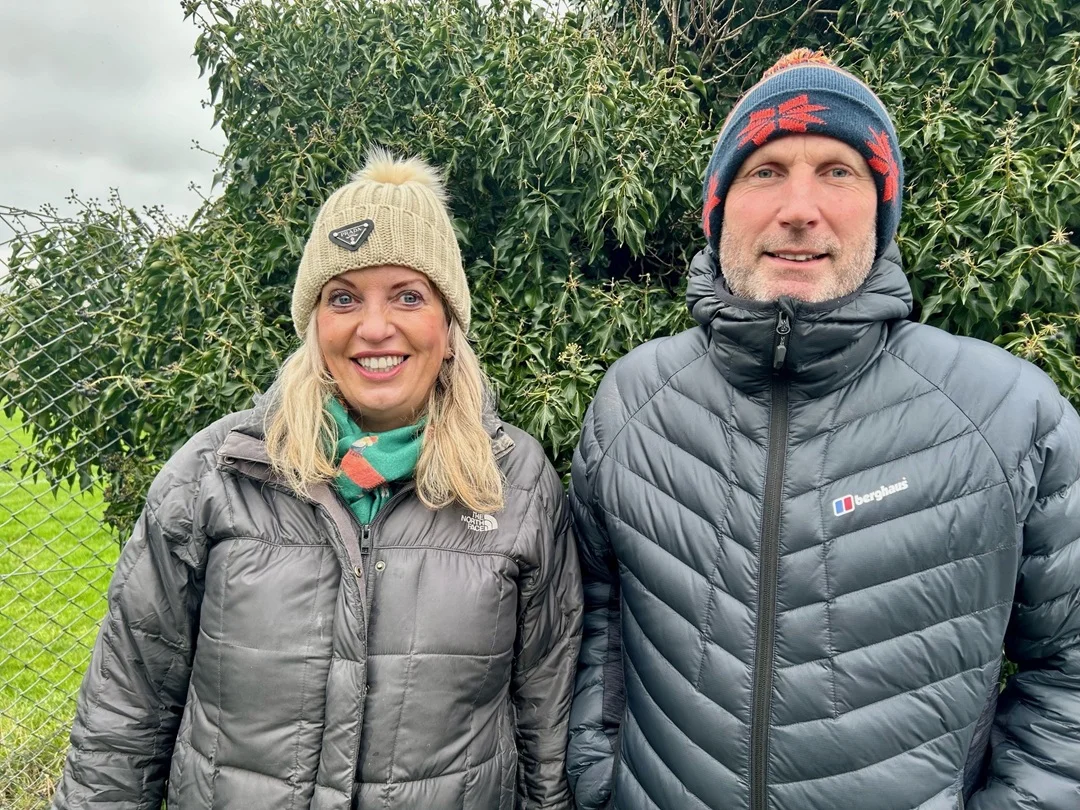Gavin and Louise stand outdoors in winter clothing with a tree in the background