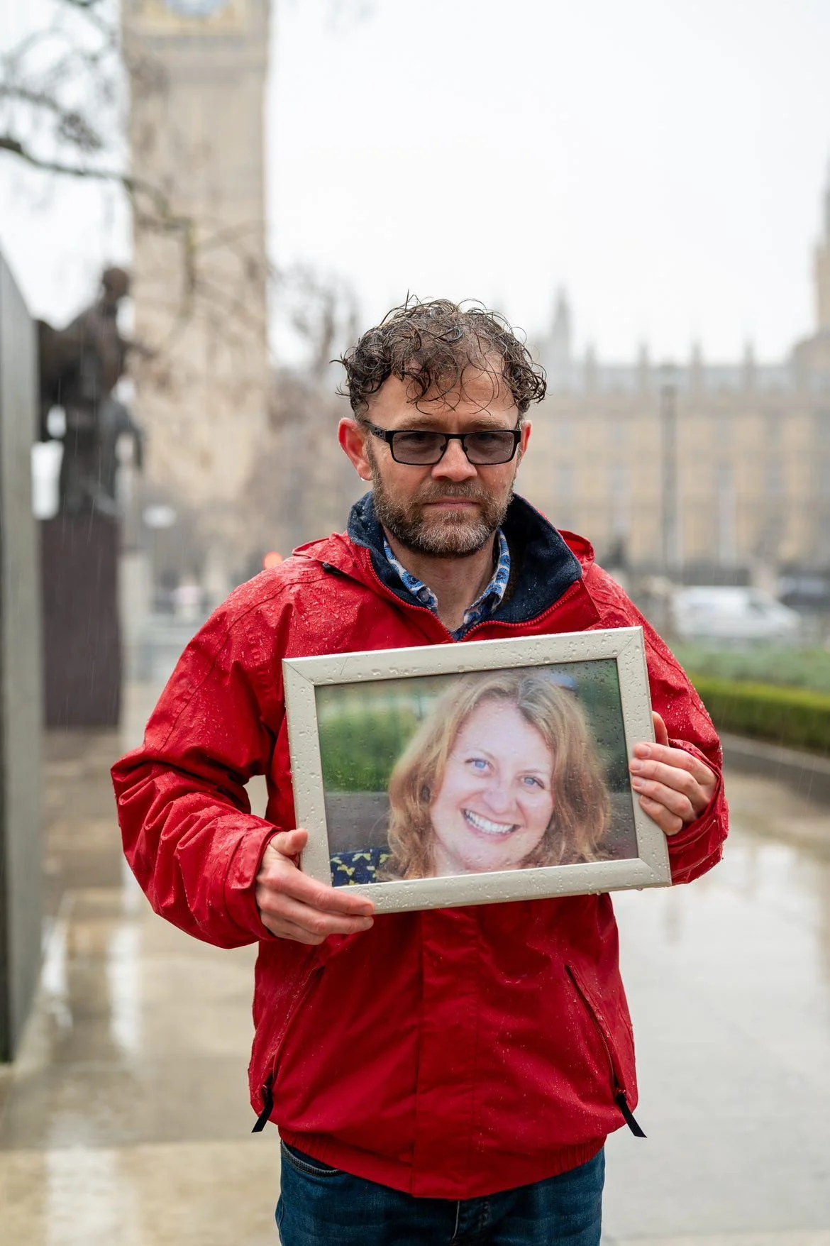 Mark Smith stands holding a picture of his late partner during an event in Westminster