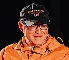 Close up of Neil Munn wearing a black cap and orange jacket